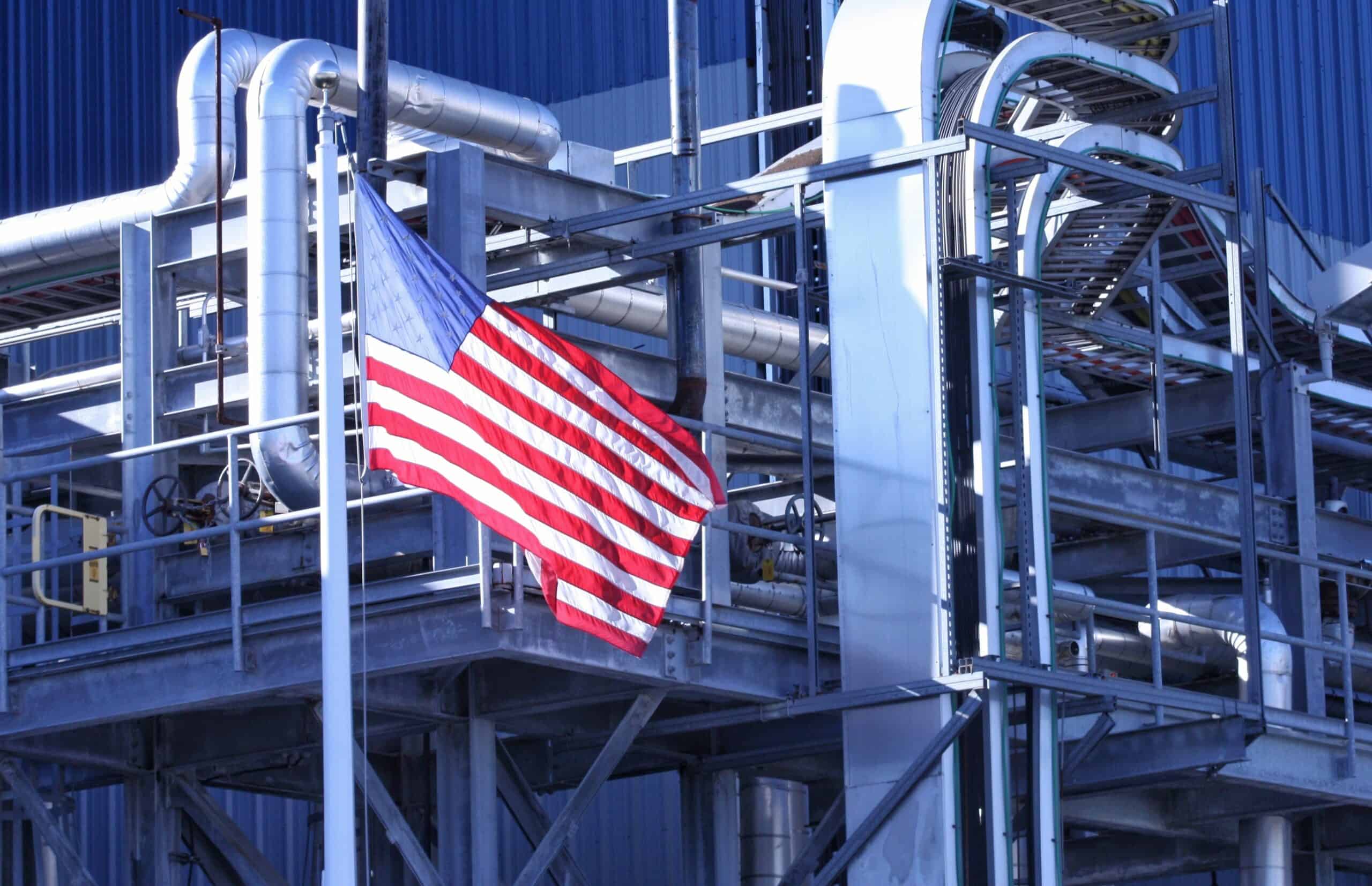 American flag flying on industrial factory pipes and structures, representing manufacturing and industrial services.