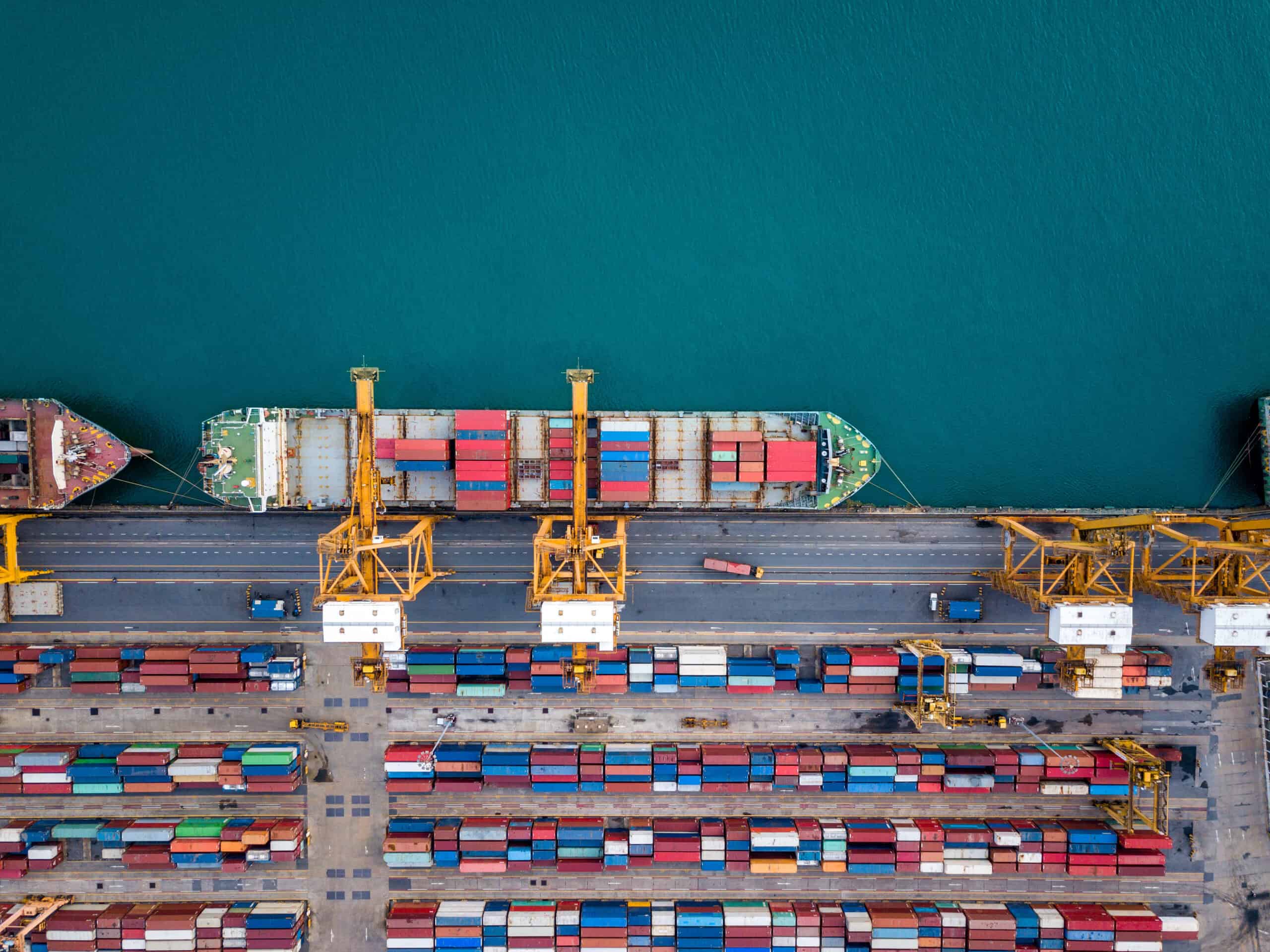 Aerial view of shipping containers and cargo ships at a busy port with cranes.