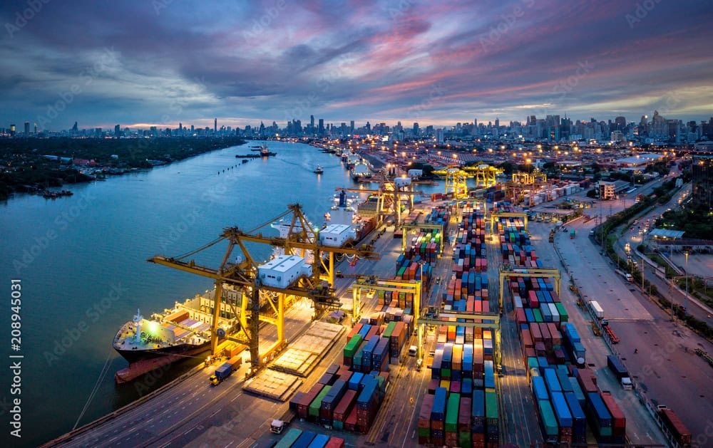 Container port with cranes, shipping vessels, and colorful containers at sunset, representing global logistics and industrial shipping.