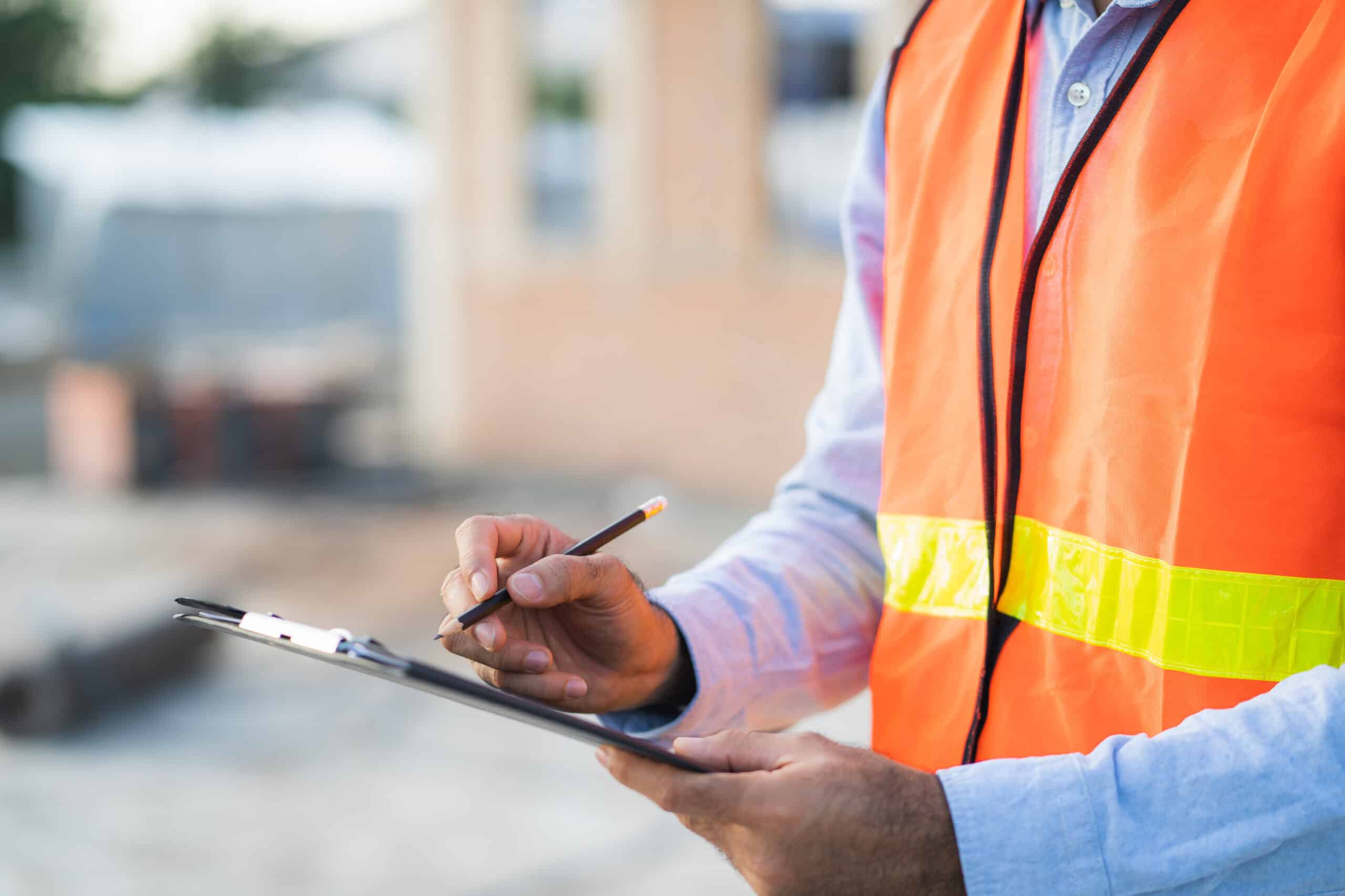 Safe construction site supervisor inspecting project progress with clipboard and pen.