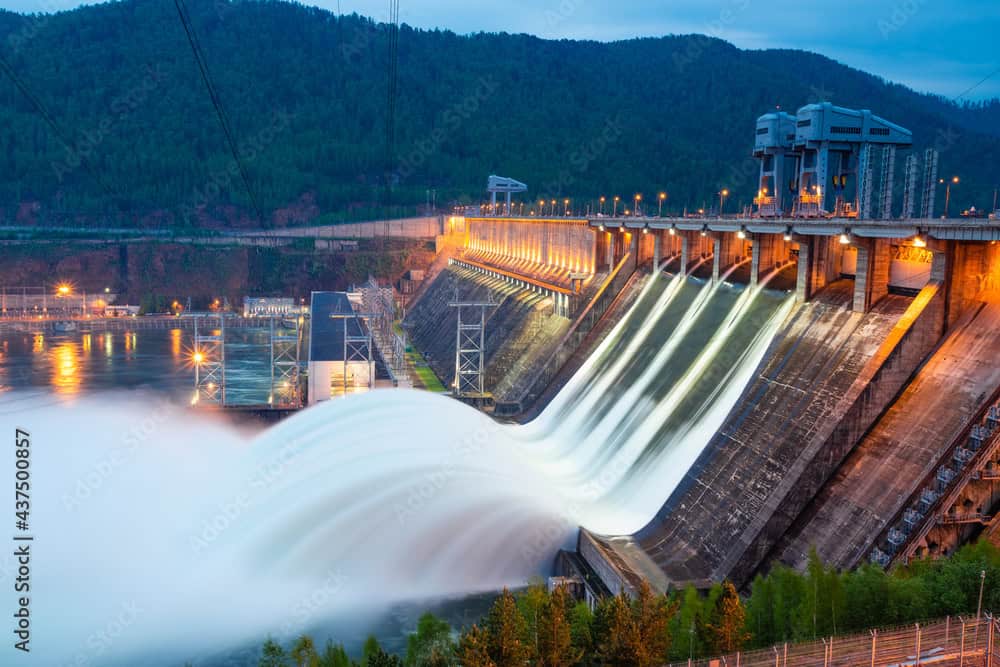 Hydropower dam with water releasing, producing renewable energy at sunset.