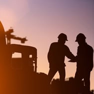 Sharp silhouette of workers shaking hands at a construction site during sunset.