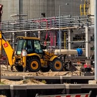 Excavator at construction site with steel structures and equipment.