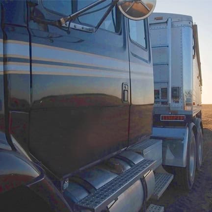 Heavy-duty black semi-truck with white and blue stripes, industrial transport vehicle at sunset.