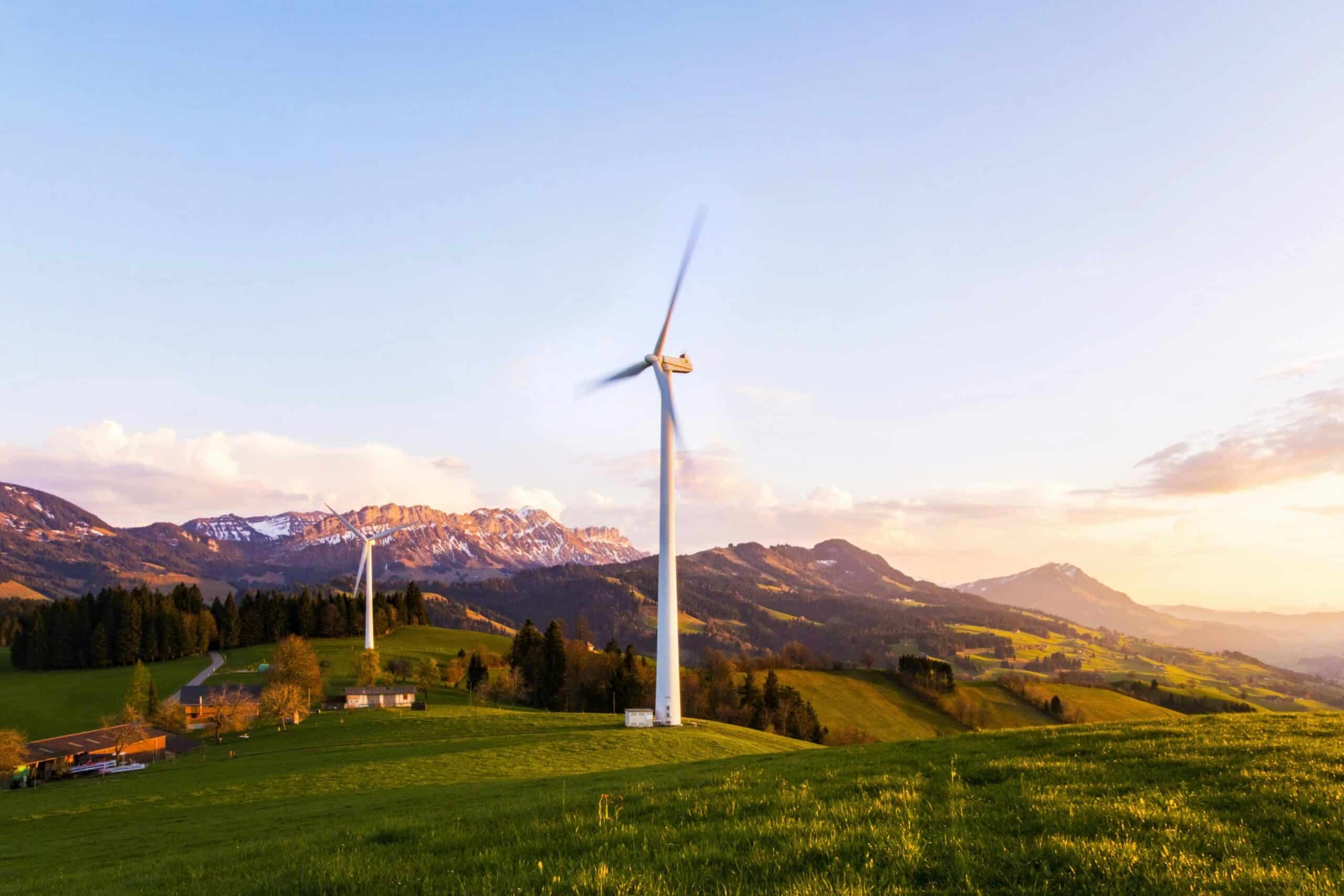 Wind turbines on green rolling hills with mountains in the background, emphasizing renewable energy and sustainable power solutions.