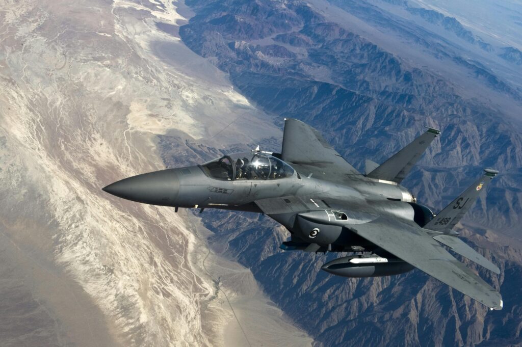 Fighter jet flying over desert mountains, showcasing advanced aviation technology.