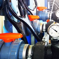 Blue industrial valves with pressure gauges and orange handles for water control.